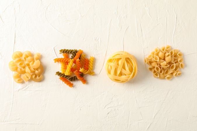 Flat lay composition with different pasta on light background, space for text. Dry uncooked whole pasta