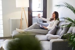 Smiling woman browsing on laptop and sitting on settee