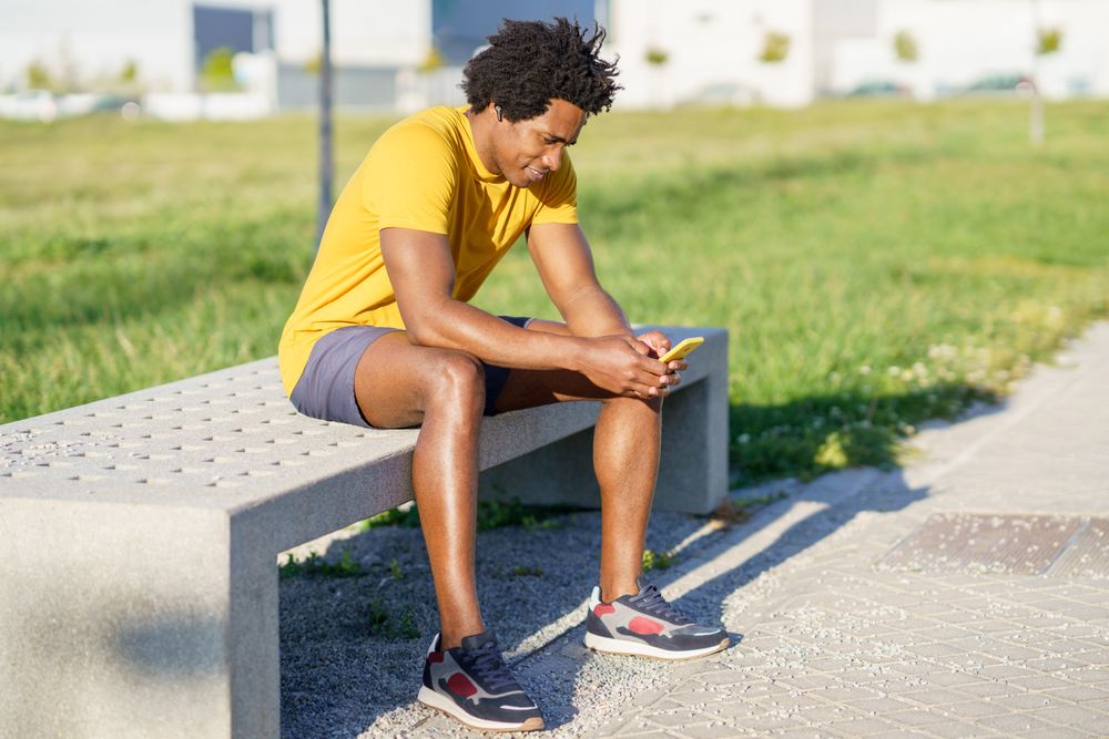 Man sitting outside looking at phone after exercising