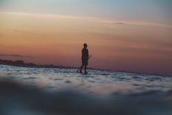 Man with paddle on surf board between waving water at sunset
