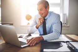 Man in business attire smiling while working at his laptop
