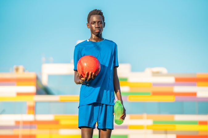 Black teenager with football ball looking at camera