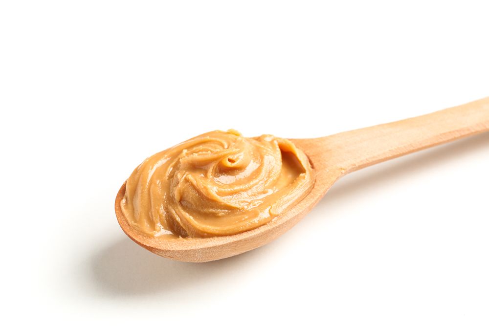 Creamy peanut butter in wooden spoon isolated on light background, closeup. A traditional product of American cuisine