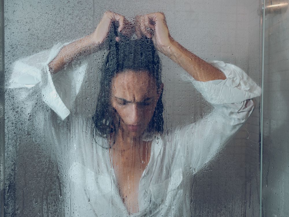 Despaired woman in wet shower cabin