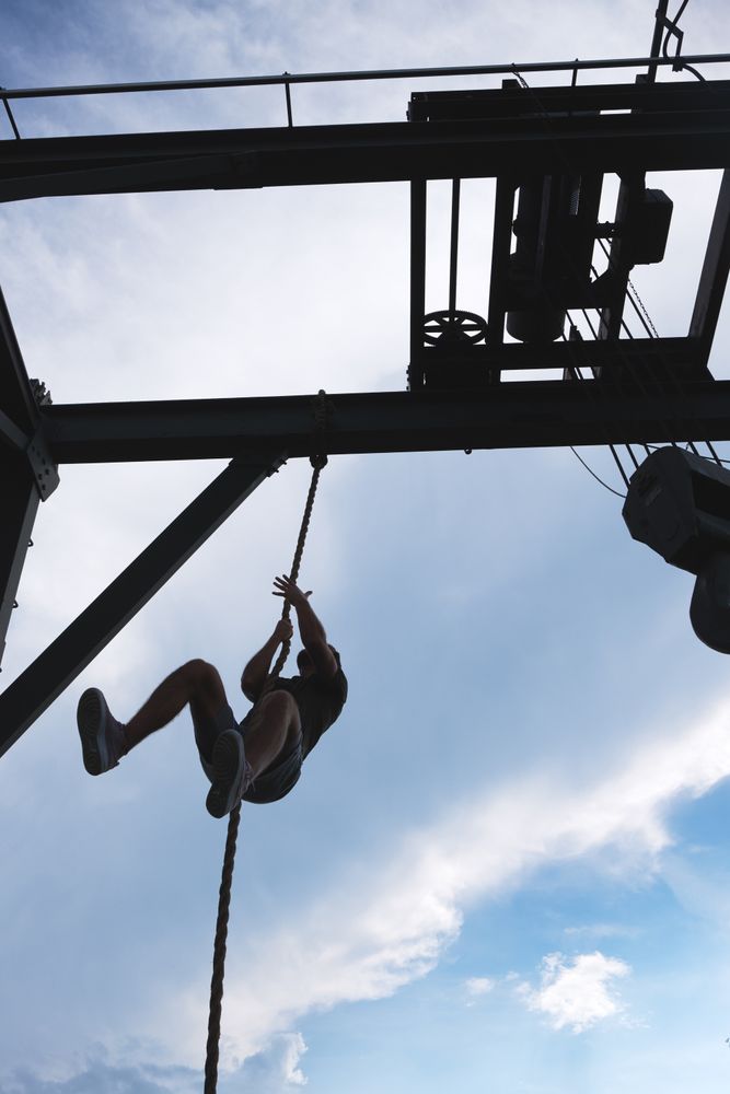 Anonymous man climbing rope in outdoor gym