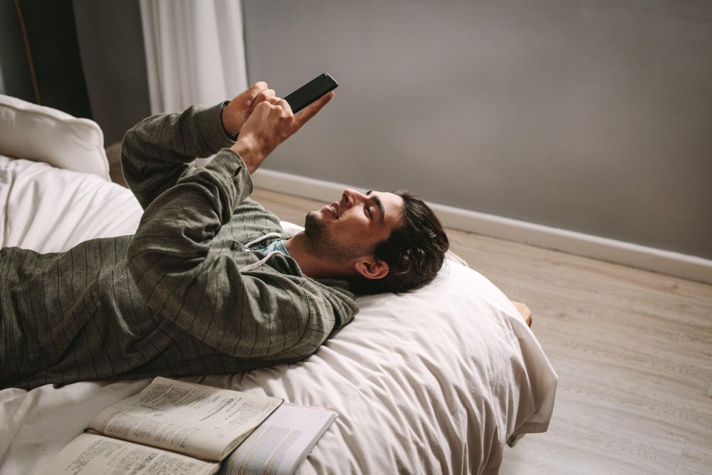 Young man using mobile phone lying on bed with books by his side - Premium  Photo (bEnBG0) - Noun Project