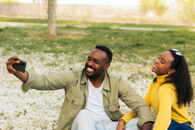Black couple taking a selfie sitting on the grass