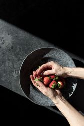 Hands with heap of strawberry near plate