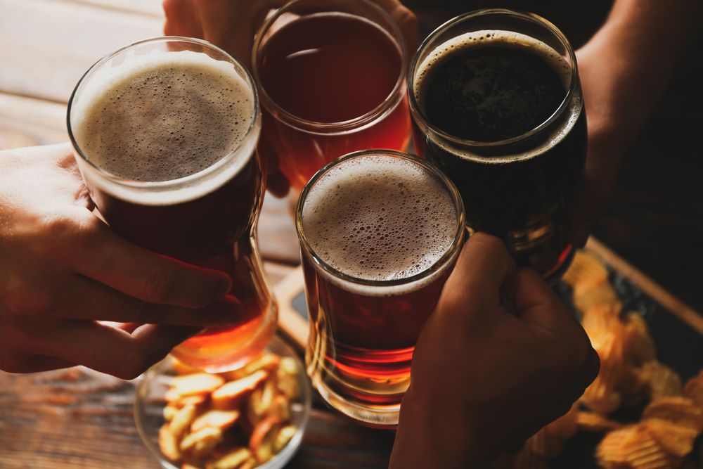 Four men cheers with beer on wooden background with snacks