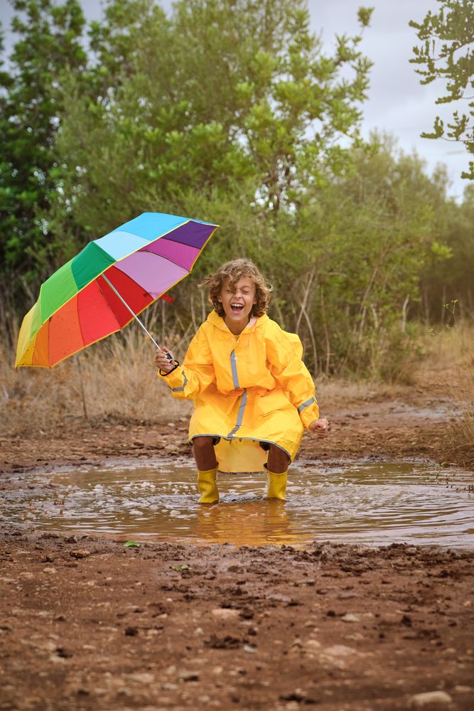 Cheerful boy with umbrella jumping in puddle