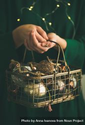 Woman in green dress holding wire basket of gold holiday decorations, vertical composition 43xOrb