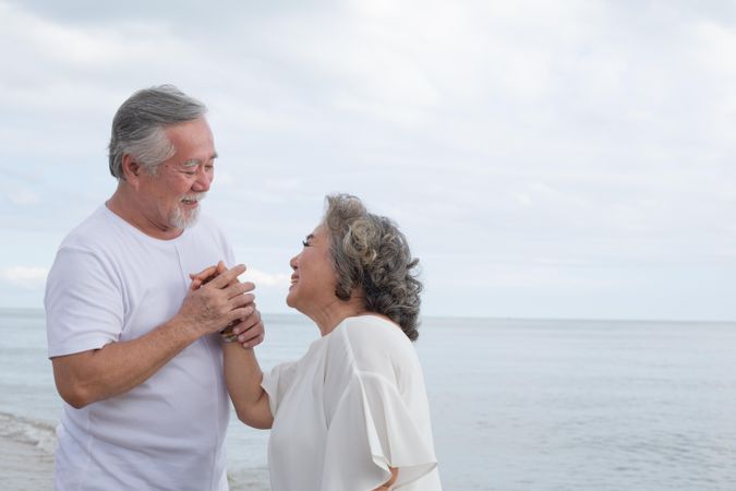 Mature Asian couple laughing together at the beach