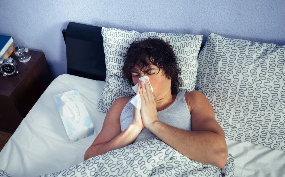Looking down at ill man sneezing in bed