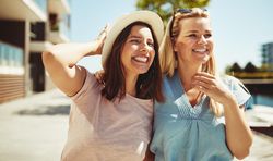 Two women smiling and strolling together on sunny day near the river