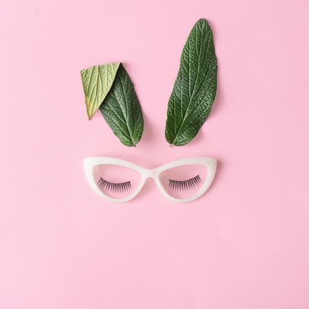 Bunny rabbit face made of natural green leaves with glasses on pastel pink background