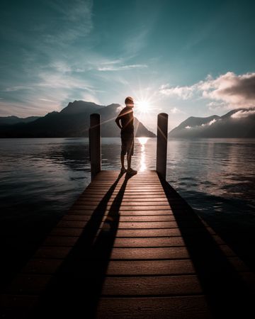 Silhouette of man standing on wooden dock during sunset