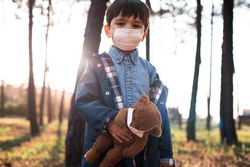 Boy holding teddy bear standing in woods