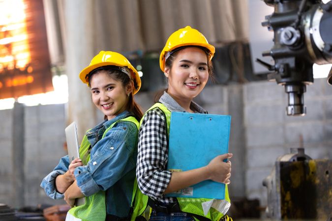 Portrait of two female engineers or technician worker holding clipboard standing back to back