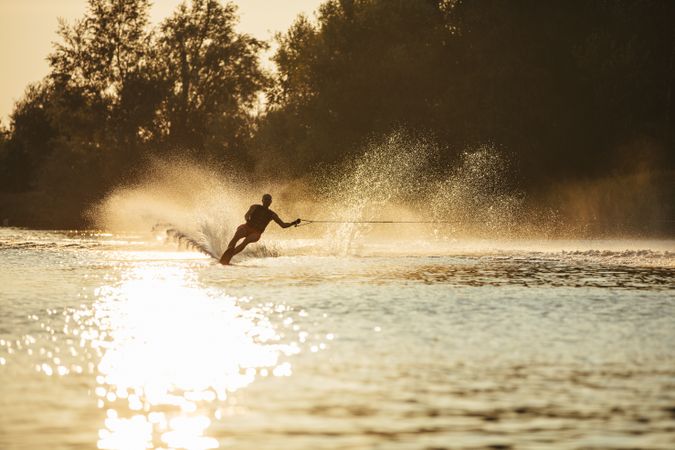 Man water skiing at sunset with one hand on tow rope