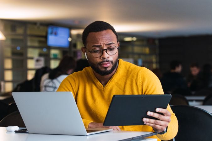 Man with earbuds using tablet and laptop at table