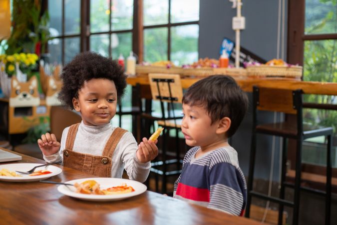 Cute Black boy sharing snacks with his friend at a cafe