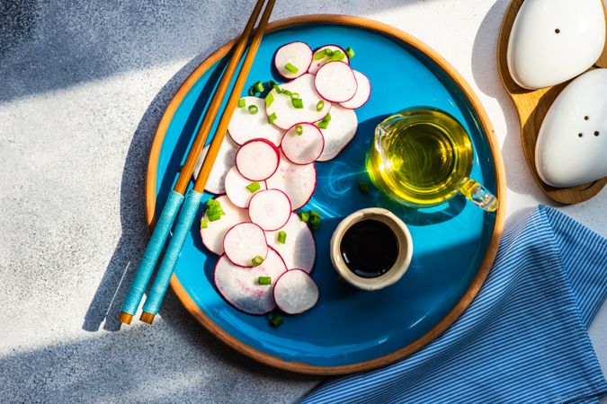 Top view of sliced radishes on blue plate served with oil