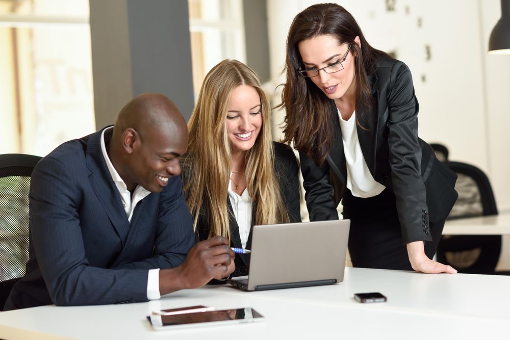 Happy colleagues working together in office around a laptop