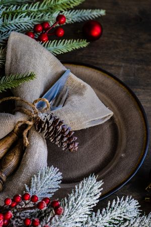 Close up of rustic table setting for Christmas nestled on table with pine and red baubles