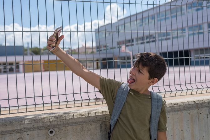 Boy taking selfie on smartphone outside of school yard