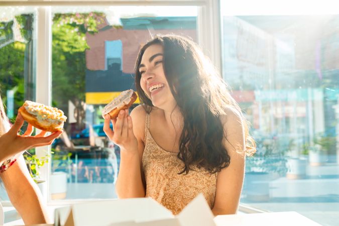 Joyful female friends eating donuts at cafe