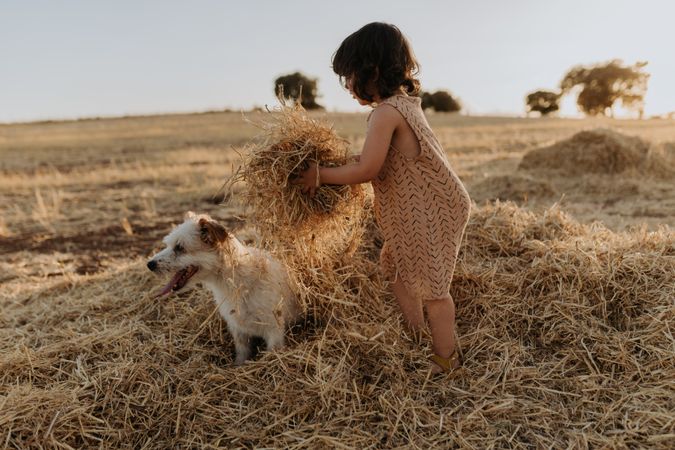 Child lifting piles of hay over her dog