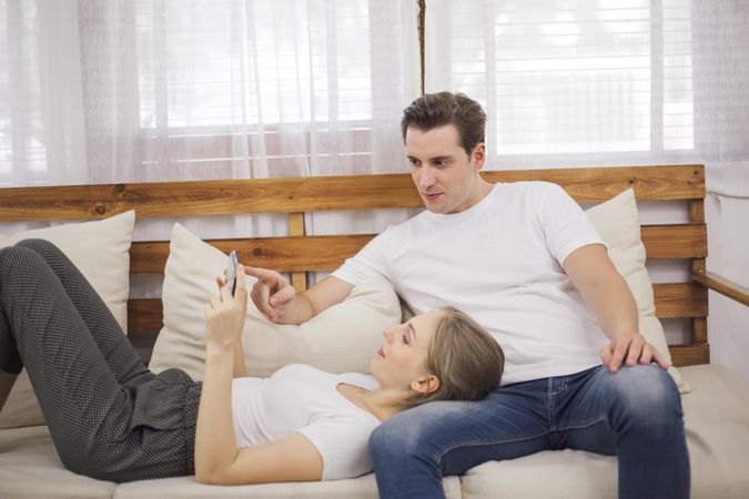 Happy couple lying on couch on smartphone
