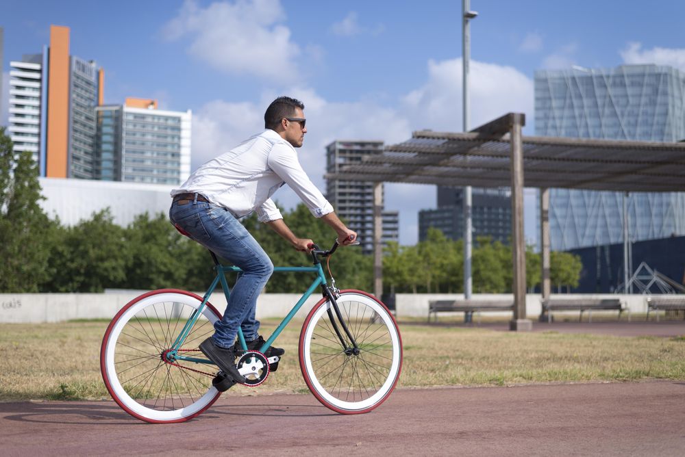 Male riding red and green bike outside next to city buildings on warm day