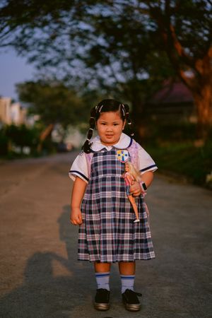 Young girl in school uniform standing on gray asphalt road