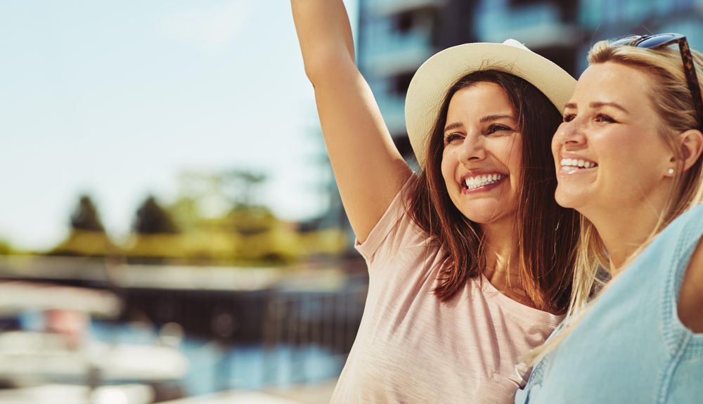 Two women laughing together with arms up on sunny day next to the river, copy space