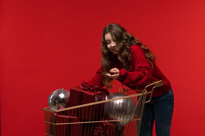 Young girl in red sweater reaches into gold shopping cart