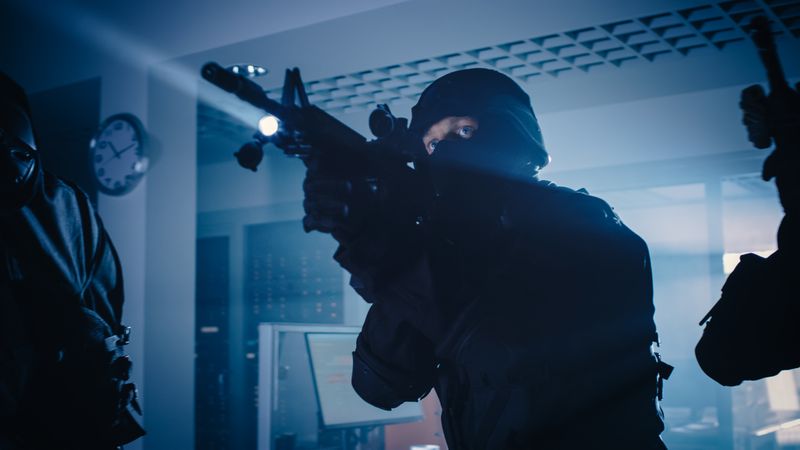 Masked Team of Armed SWAT Police Officers Move in a Hall of a Dark Seized Office Building with Desks and Computers.