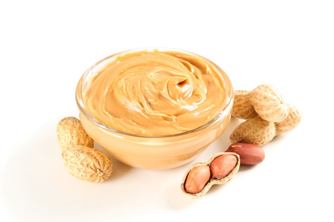 Creamy peanut butter in glass bowl and peanut isolated on light background. A traditional product of American cuisine