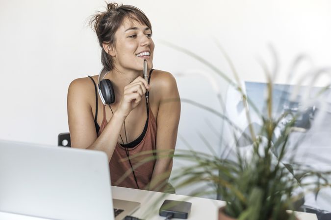 Happy woman sitting at desk with pen to her mouth