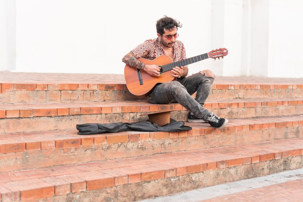 Latin musician sitting on the sidewalk playing guitar for cash