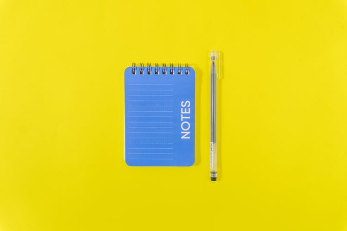 Flat lay of a pen and notebook on a vibrant yellow background