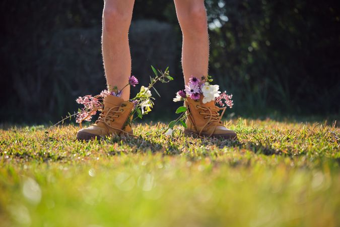 Crop person wearing boots with flowers standing on meadow
