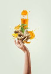 Women hand holding balancing ginger and orange immunity boosting drink with splashing and ingredients at light background. Creative healthy lifestyle. Levitation food . Front view