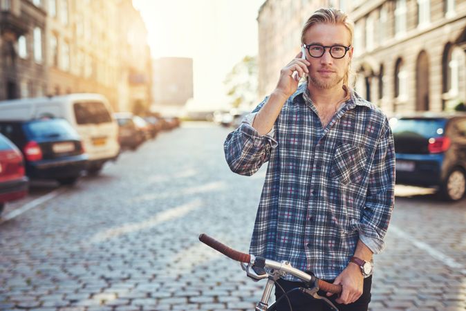 Man in glasses on his cellphone on a European cobble street with bicycle