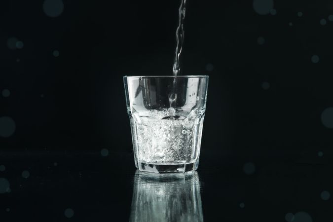 Dark room with glass of water being poured, copy space
