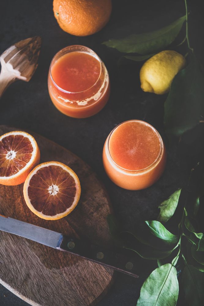 Two glasses of freshly squeezed blood orange juice, with squeezer, and fruit, top view