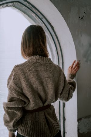 Back view of woman in gray sweater standing by the window