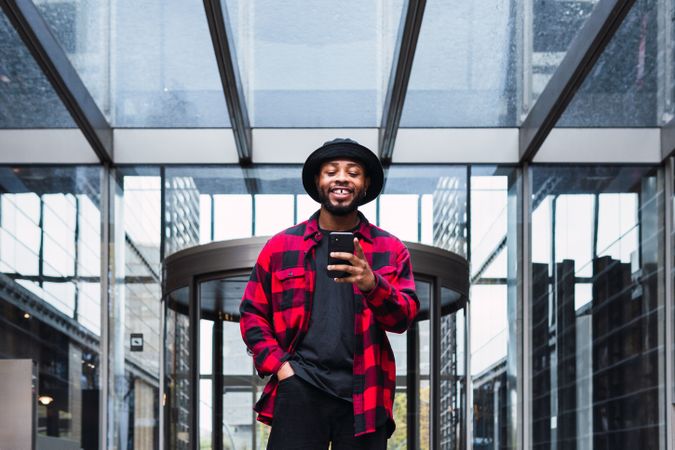 Cheerful Black male with smartphone in contemporary building