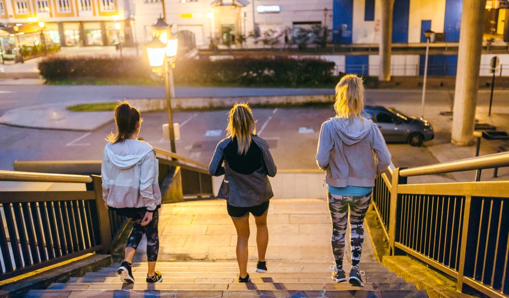 Back of female friends training running down stairs in city at night