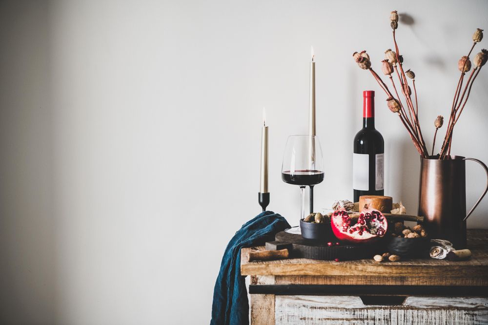 Rustic setting of wine, cheese, long candles, with pomegranate, and dried poppies, with copy space